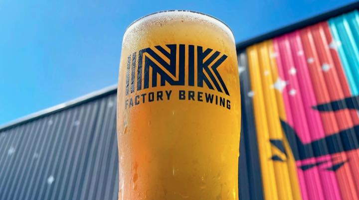 Ink Factory Brewing beer glass in front of a colorful Jacksonville Beach mural.
