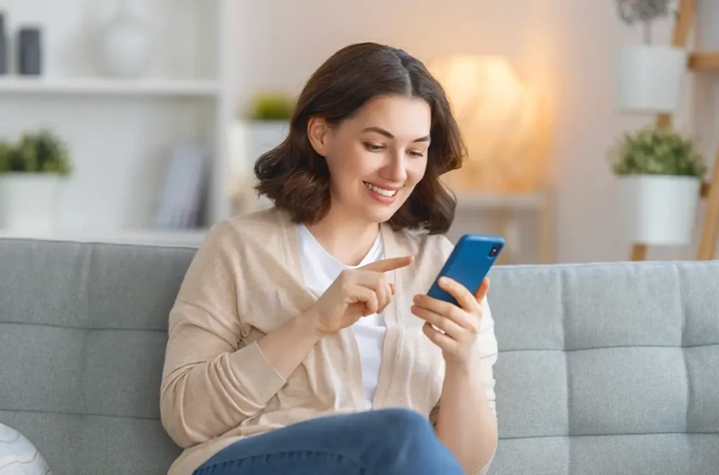 A woman sits on her couch, looking at her phone. New restaurant ordering technology allows her to request a text to her phone to place and order online instead.