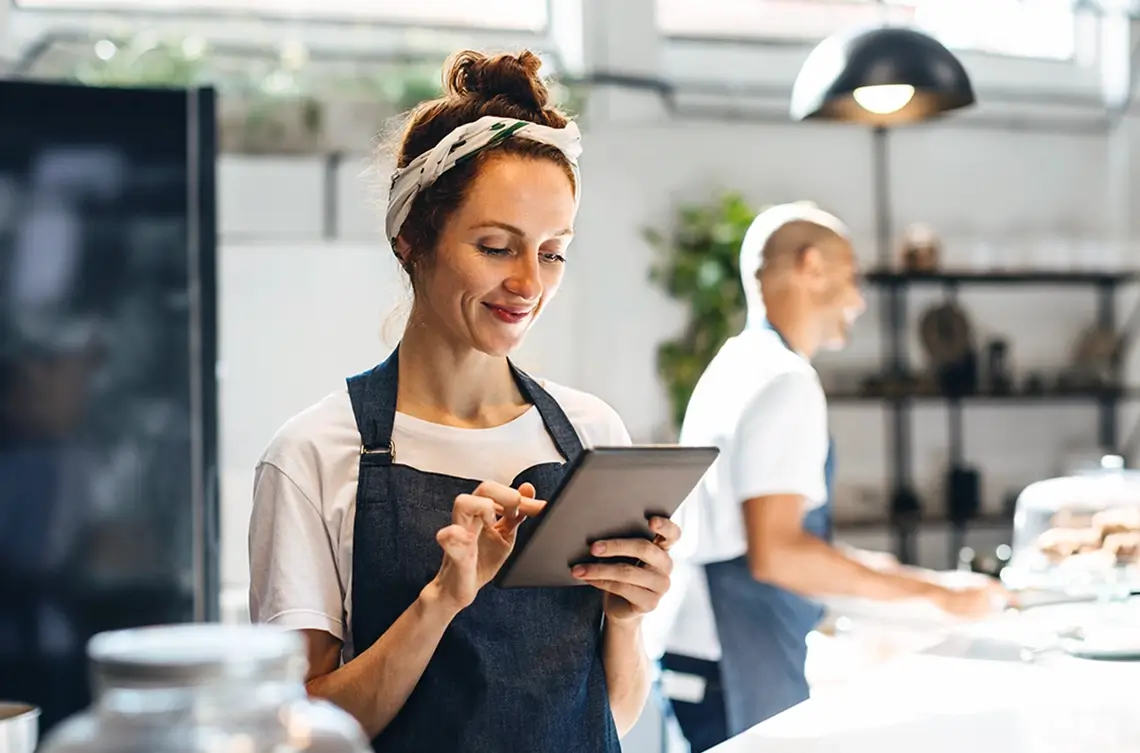 A woman evaluates her restaurant efficiency on her tablet utilizing AI tools.