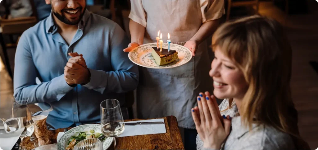 One way to grow a restaurant business is to keep guests coming back by providing them with unforgettable experiences, like this waiter is doing as they serve a slice of cake with candles to the birthday girl!